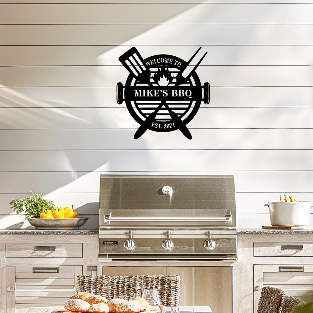 Metal wall art with 'Welcome to Mike's BBQ' text above a barbecue grill in a kitchen setting. Personalized text and date