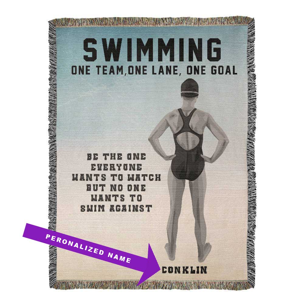 A personalized woven blanket with a swimmer's back view on it, featuring the text 'SWIMMING ONE TEAM, ONE LANE, ONE GOAL' along with a motivational quote and the name 'THOMSON'. The blanket has decorative fringe on the sides. The name is customizable.