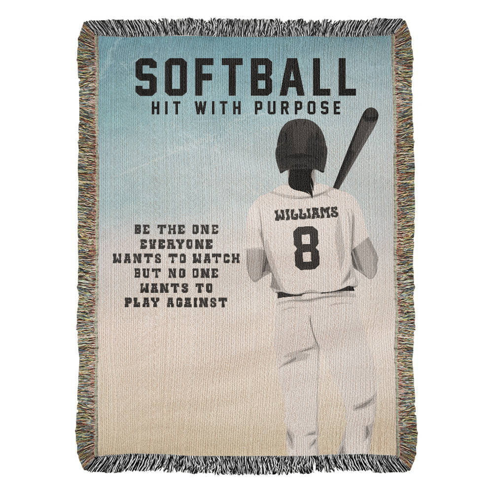 A woven blanket with a girls softball theme, featuring a player in the batter's box, and the text 'SOFTBALL HIT WITH PURPOSE' along with the encourage ment 'BE THE ONE EVERYONE WANTS TO WATCH BUT NO ONE WANTS TO PLAY AGAINST'.