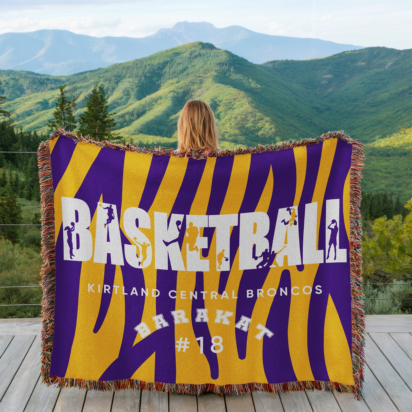 Person holding a basketball-themed blanket with mountains in the background