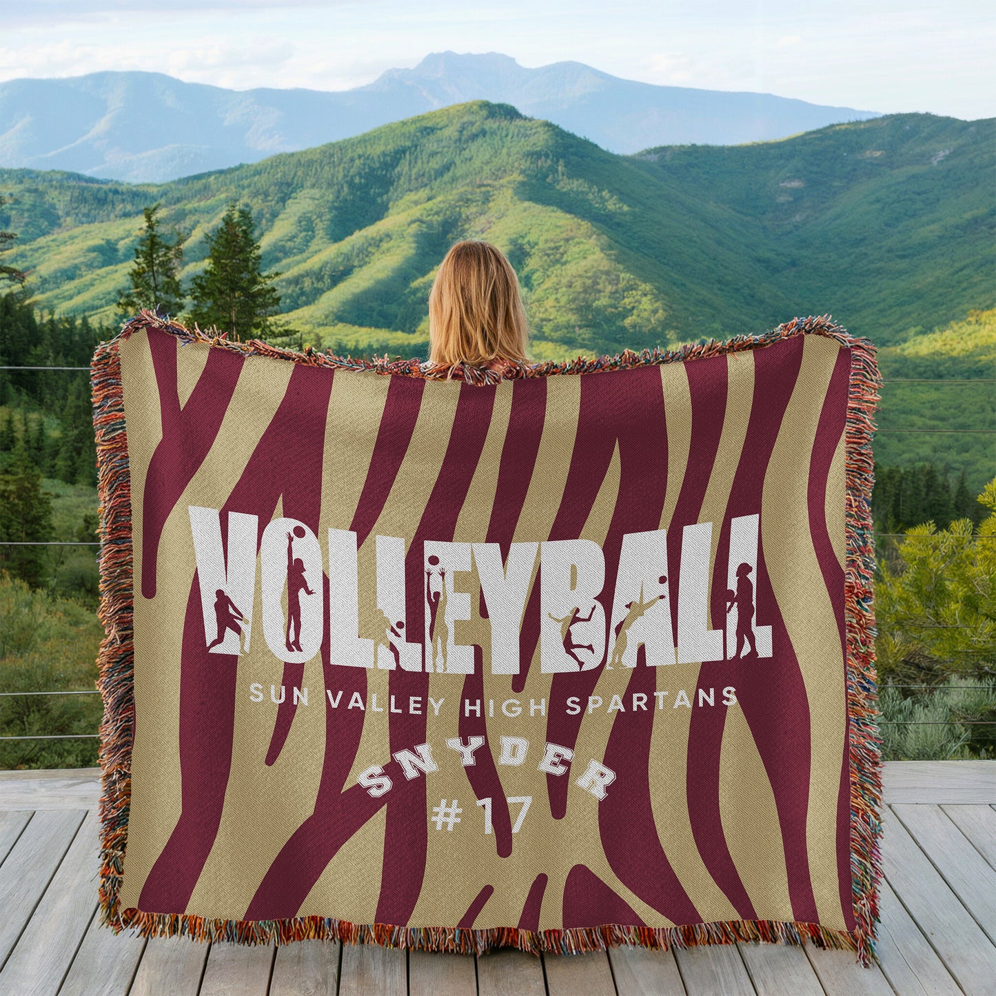 Person holding a 'Volleyball' themed blanket with mountainous landscape in the background