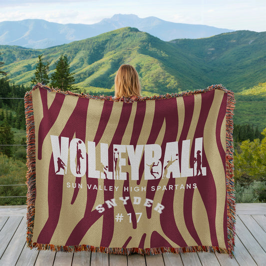 Person holding a 'Volleyball' themed blanket with mountainous landscape in the background