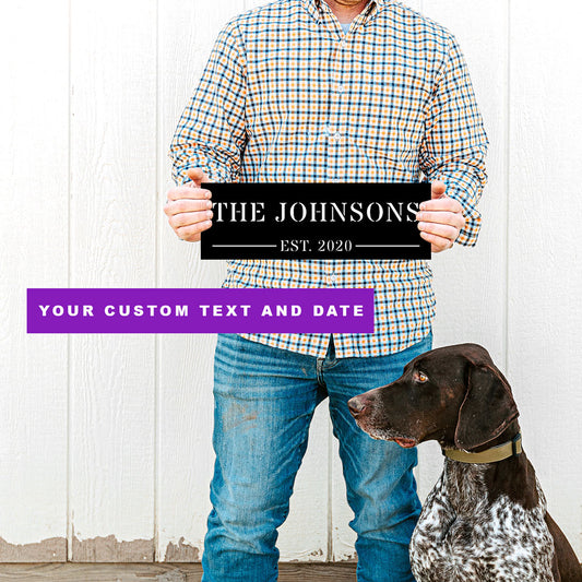 Man holding a personalized metal wall art sign with 'The Johnsons' and a dog sitting next to him. The name and date are customizable by FunLifeNow.com