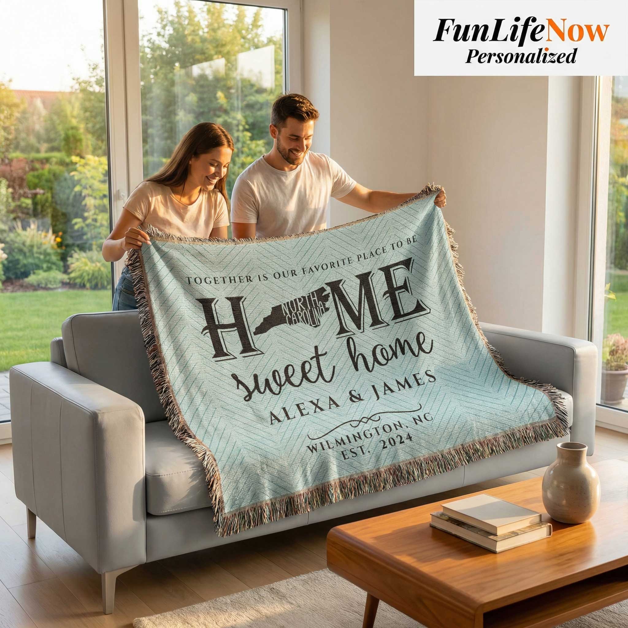 Couple holding a personalized blanket with 'Home Sweet Home' text in a living room.