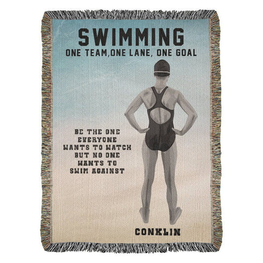 A woven blanket with a swimmer on it, featuring the text 'SWIMMING ONE TEAM, ONE LANE, ONE GOAL' and the name 'CONKLIN'.
