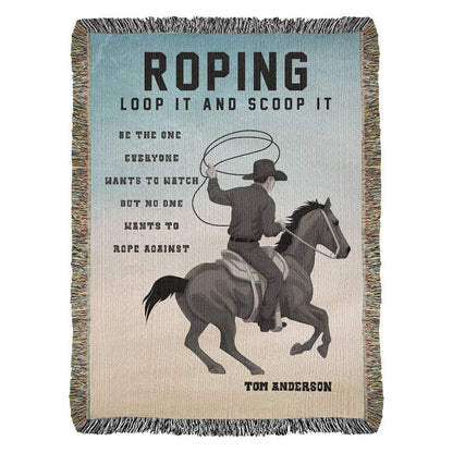A woven blanket with a printed design featuring a cowboy on a horse with a lasso, and the text 'ROPING LOOP IT AND SCOOP IT' along with the signature of a personalized name at the bottom.