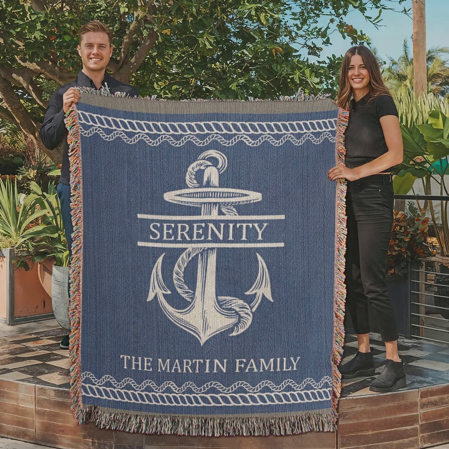 A woven blanket with a rope-wrapped anchor design, customized with the personalized text 'Serenity' and personalized text 'The Martin Family', in blue and natural color tones with fringe detailing. Blanket available at Funlifenow.com